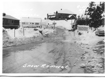 A black and white image of State Route 158 in June Lake showing a freshly plowed road. Writing on the image reads "Snow Removal. 2-11-62. C.F.S. M-1419."