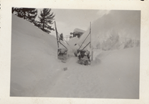 An undated black and white image showing a snowblower removing snow for the road. The vehicle is surrounding on all sides by heavy snow.
