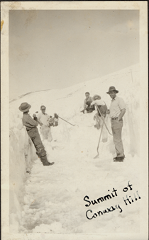 An undated black and white image of men resting as they clear snow from the highway using snow shovels. Writing on the picture reads "Summit of Conway Hill."