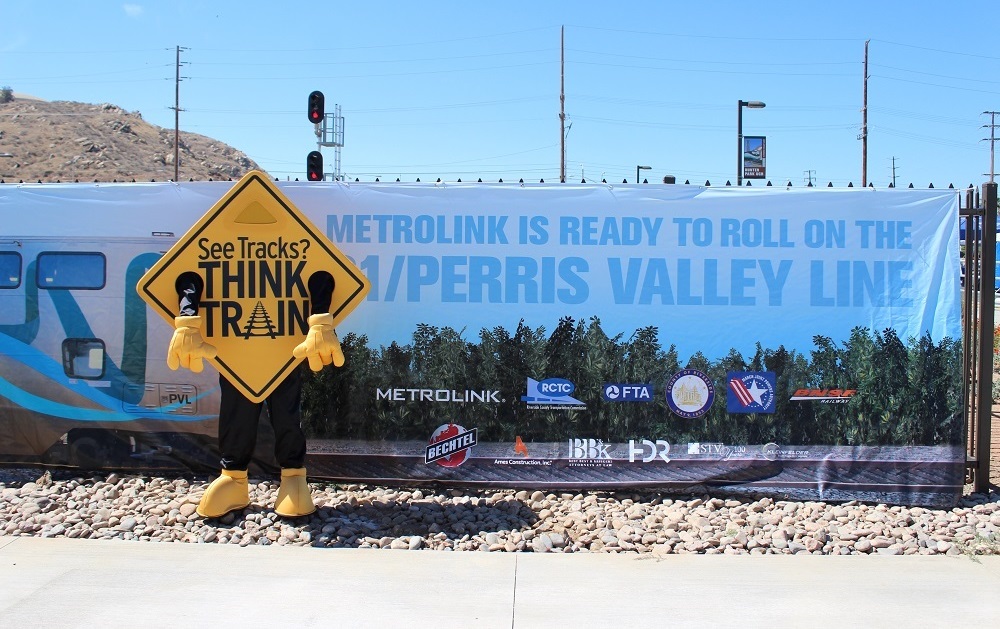 A large sign with information about the MetroLink program with a mascot dressed as a railroad sign in the foreground.