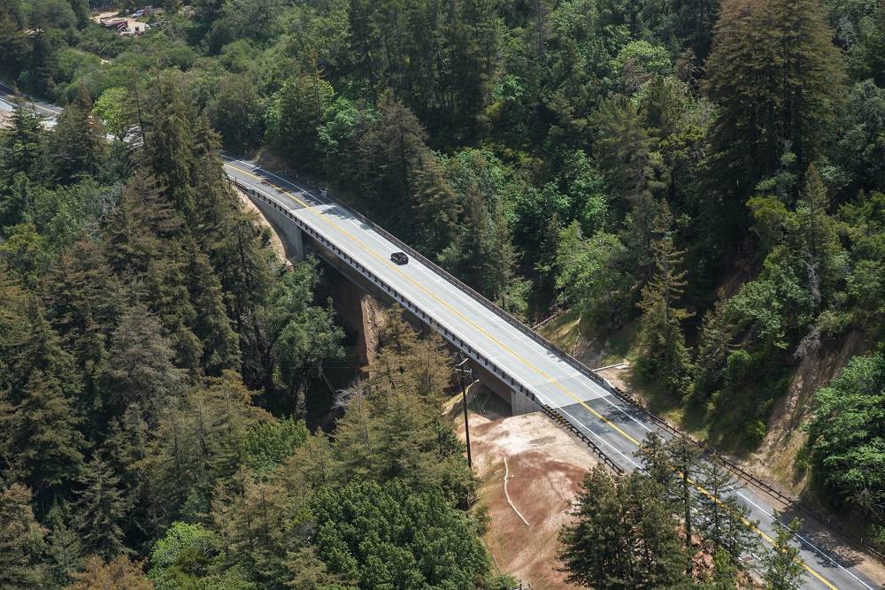 From above, a view of a highway bridge spanning a large tree-filled valley.