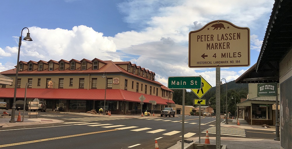 View of a newly paved 4 way intersection with a sign indicating the way to the historical landmark 'Peter Lassen Marker'.