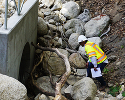 Photo of a Caltrans inspector looking over a newly installed culvert.