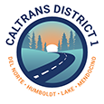 Caltrans District 1 shield. Humboldt, Del Norte, Lake, Mendocino. The sun sets over a road that winds from the foreground to the background. Mountains line each side.