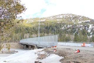 Photo of the finished west half of the Cisco Grove Overcrossing on I-80. The photo was taken in March 2022 and snow is still on the ground. Mesh fencing runs the length of the overcrossing and a mountain imprint has been stamped into the concrete on the side of the bridge structure. 