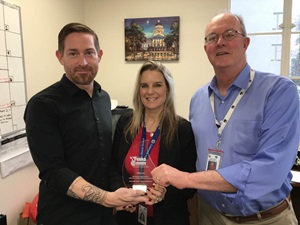 Mile Marker graphic designer Daniel DeFoe, left, and Editor Steve Breen join with Assistant Deputy Director of Public Affairs Tamie McGowen in displaying the TransComm award.