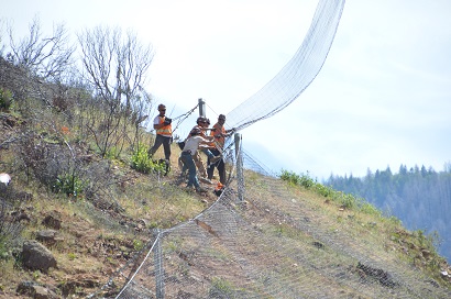 Workers grab a wire mesh – some segments of which were as large as 12 feet wide and 120 feet long – being delivered by helicopter along State Route 70. Workers grab a wire mesh – some segments of which were as large as 12 feet wide and 120 feet long – being delivered by helicopter along State Route 70.