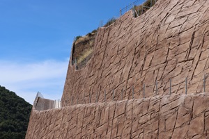 Large brown retaining wall looms in the foreground with blue skies behind. 