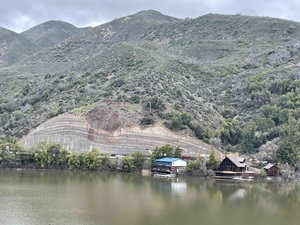 Aerial view of state route 20 near Blue Lakes. Construction equipment is at work on ta large retaining wall. Clear Lake is visible in the foreground and a mountain rises in the background. 