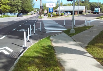 A roadway intersects with another. At the right turn, temporary bollards are installed to simulate a wider curb area.