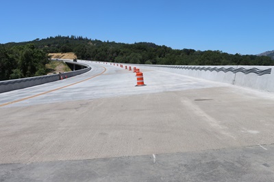 The new Calpella Bridge lined with orange delineators. The walls are stamped concrete with a wave pattern. 