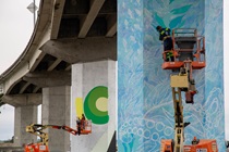 Artists Laci Dane of Wiyot and Jessica Cherry of Crescent City work from lifts to paint murals on two of the columns of the Samoa Bridge in Eureka.