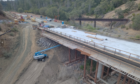 Heavy equipment works beneath a partially built bridge deck. 