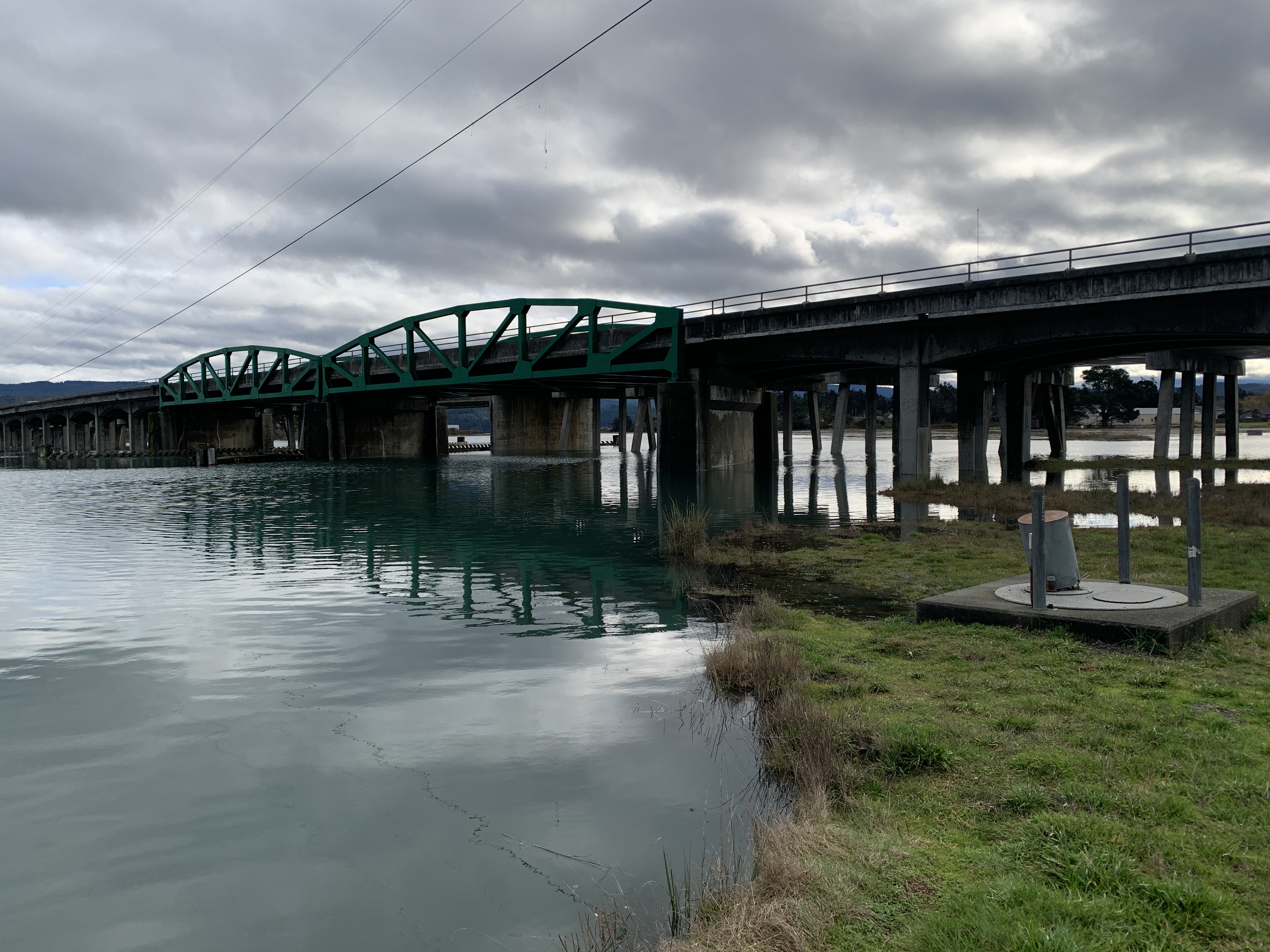 Eureka Slough Bridge looking west. Concrete pillars extend from under the bridge deck into the green water of the Eureka Slough. 