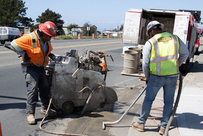 Contractors with Ghilotti Construction work along the roadway with an industrial wetvac. 