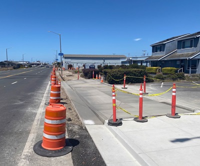Newly poured sidewalks are blocked by orange cones. 
