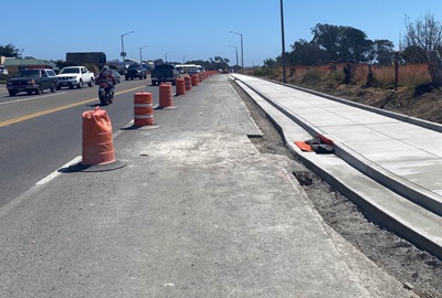 Newly poured sidewalks are protected by orange cones. Traffic continues unimpeded on the nearby roadway.