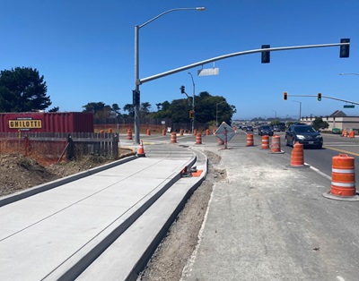 Newly poured sidewalks are protected by orange cones. A stoplight stands watch over flowing traffic. 