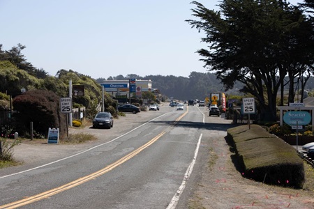 Route 1 in Gualala, Mendocino County, is framed by a mix of green leafed trees, residences, and businesses including a gas station and motel. 