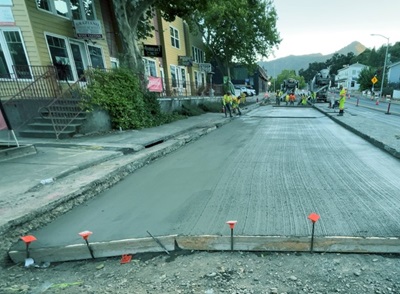 A construction crew of about 9 wearing yellow high visibility gear smooth freshly poured concrete on US 101 in Hopland.