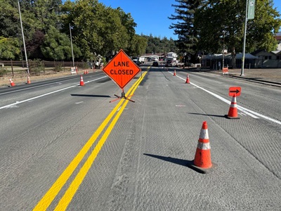 Exposed road surface with cones indicating travel lanes and a lane closed sign.