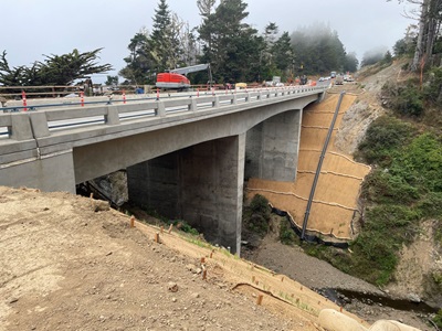 Heavy equipment on one side of Jack Peters Creek Bridge on Route 1 in Mendocino County. The bridge's abutments and columns stand against brown erosion control barrier. 