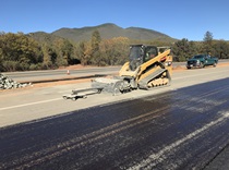 Repaving work on State Route 29 as part of the Konocti Corridor Improvement Project. Low mountains are visible in the distance underneath a blue sky.