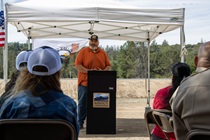 Lake County District 1 Supervisor Moke Simon stands at a lectern under a white shade structure, addressing a group of partners and supporters of the Konocti Corridor Improvement Project. 