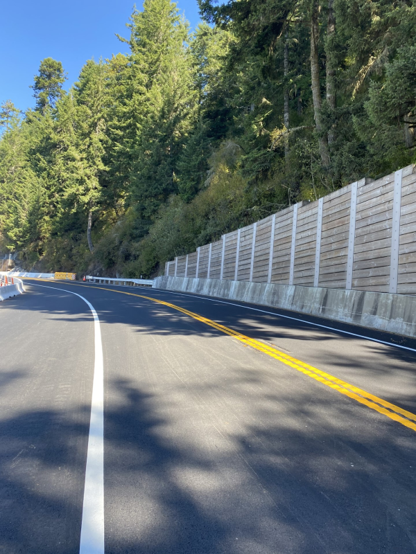Curved stretch of U.S. 101 at Last Chance Grade in Del Norte County. A retaining wall towers over the cement roadway.