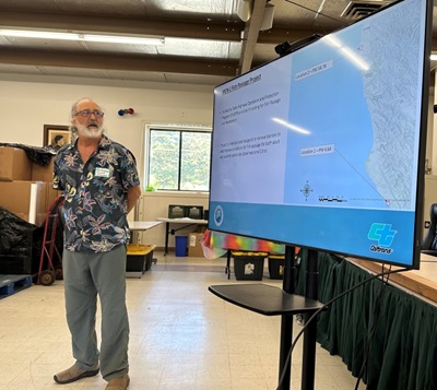Caltrans staff person gestures toward a screen with a map showing two locations on Route 1 in Mendocino County and the label Mendocino 1 Fish Passage Project