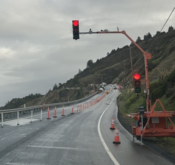Red light shines above wet pavement on State Route 1 in Mendocino County. Signalized one-way traffic control in effect as one lane is closed for construction.