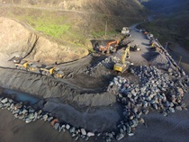 Aerial shots of heavy equipment moving large boulders into place along the ocean under Route 1 in Mendocino County. 