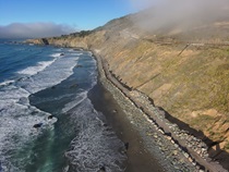 State Route 1 runs along the Mendocino Coast. This stretch of coastline has a boulder wall buttressing the hillside and road above. 