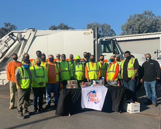 Group of people wearing reflective safety vests holding a "Back to Work" sign. For more information, call (619) 688-6670 or email CT.Public.Information.D11@dot.ca.gov