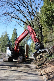 A large piece of equipment with a claw-like attachment known as a grapple reaches to remove vegetation along a portion of State Route 174 in Nevada County.