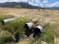 Photo showing three culvert drains that extend from underneath SR-49 in Sierra County. A small puddle of water is seen in the foreground, while a cone is placed along the shoulder of the highway near the top of the photo to mark the location of a sinkhole.