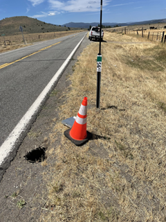 Photo showing a small sinkhole that has formed along the shoulder of SR-49 west of Loyalton in Sierra County. The sinkhole is not impacting the highway and has a cone placed next to it to mark the location. 