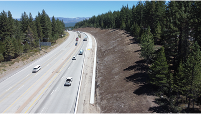 An aerial drone photo shows a cleared eastbound slope and the right shoulder of I-80 blocked off behind temporary concrete barriers known as k-rail. A new eastbound acceleration lane is being construction in this area. 