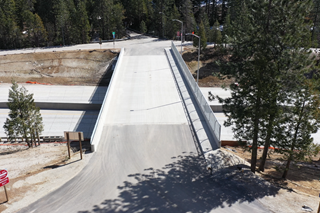 An aerial drone photo shows the newly reconstructed Drum Forebay bridge that crosses over I-80 in Placer County. The structure has one lane in each direction with a sidewalk and metal decorative fencing along the right side of the structure.