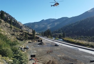 A helicopter picks up wire mesh drapery from a staging area on I-80 for placement along the westbound mountain slope. 