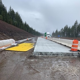 Photo showing the Central Truckee eastbound I-80 off-ramp that is in the process of being reconstructed. New concrete slabs are being poured segments at a time with concrete barriers separating the ramp from traffic.