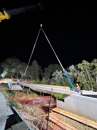 Crews installing concrete girders for the new pedestrian bridge over Rock Creek along State Route 49.