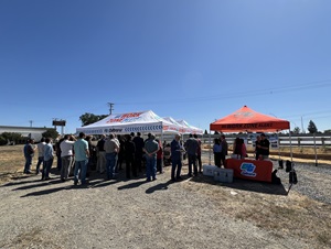 Large group of people gathering for a ribbon cutting ceremony, standing under a white pop-up tent that says Be Work Zone Alert.