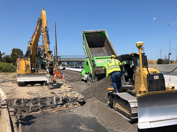 Photo of construction crews placing roadway base material in the freeway shoulder