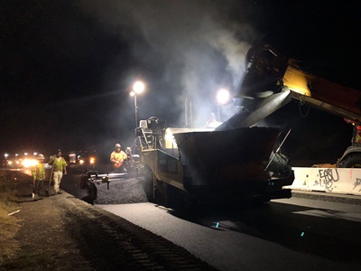 Construction crews performing nighttime paving in the freeway shoulder