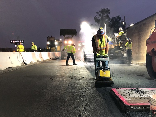 Construction crews paving in the freeway shoulder