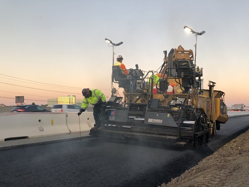 Construction crews paving in the freeway shoulder