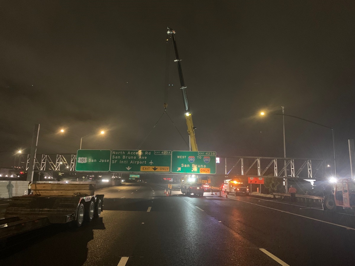 Image shows crane preparing to lift and place replacement sign bridge at night.