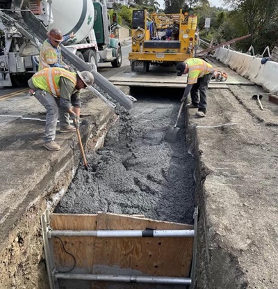 Two Caltrans employees use shovels to help fill a trench with concrete on State Route 131 in Marin County.