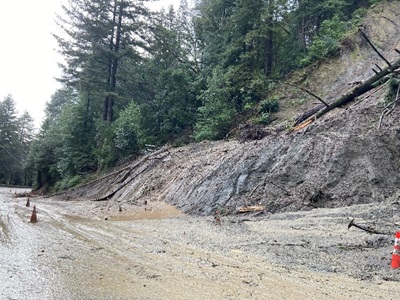 Photograph of State Route 9 with mudslide debris spilling on the roadway from a hillside on the right side of the picture.